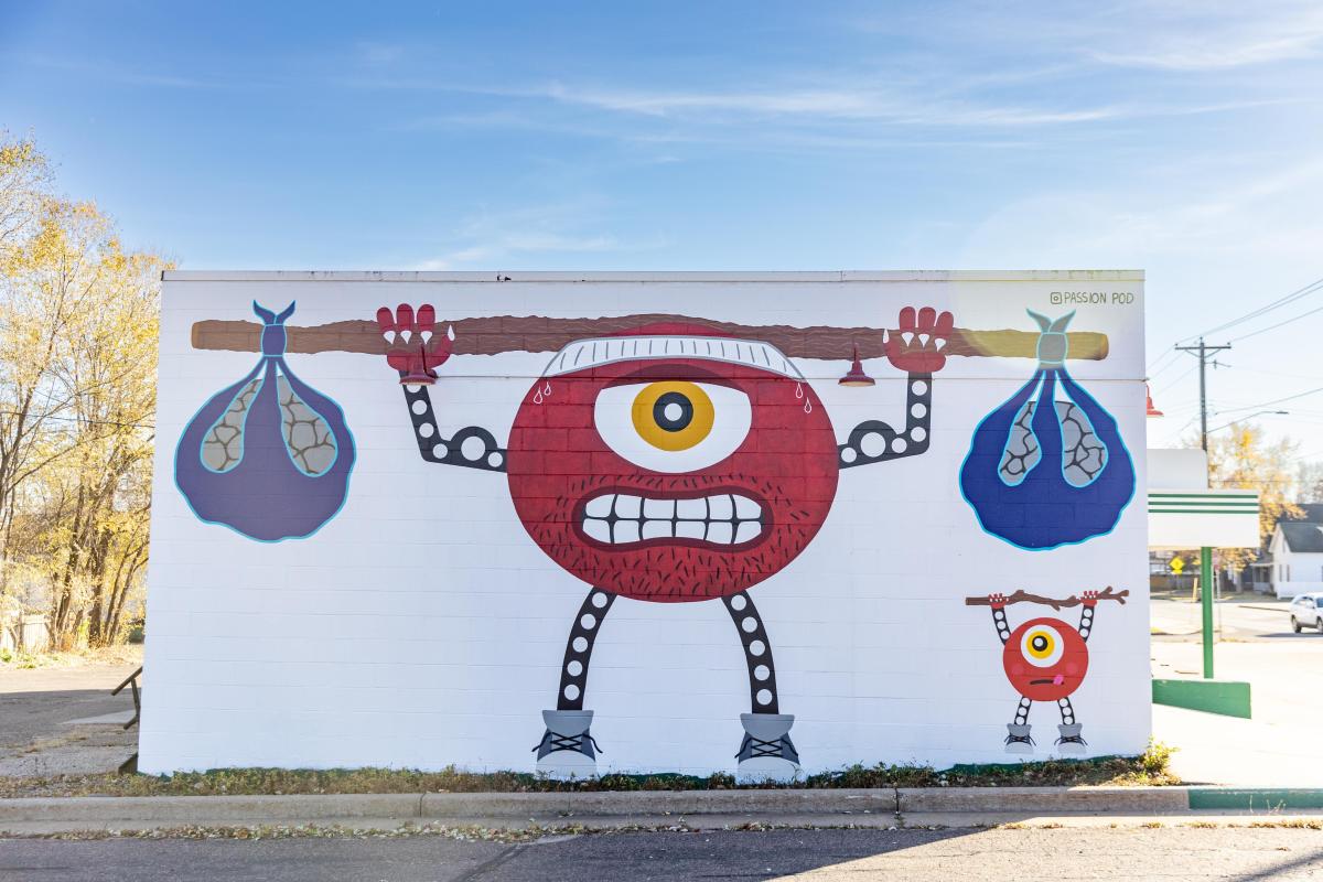 A mural of a little red weighlifting character at 5th Row Lifting Company