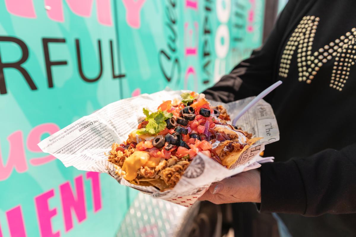 A person holding a big boat of nachos from a food truck