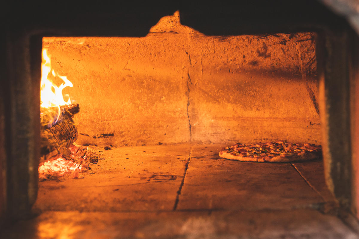 a pizza cooking next to fire in the oven at Foster's Fireside