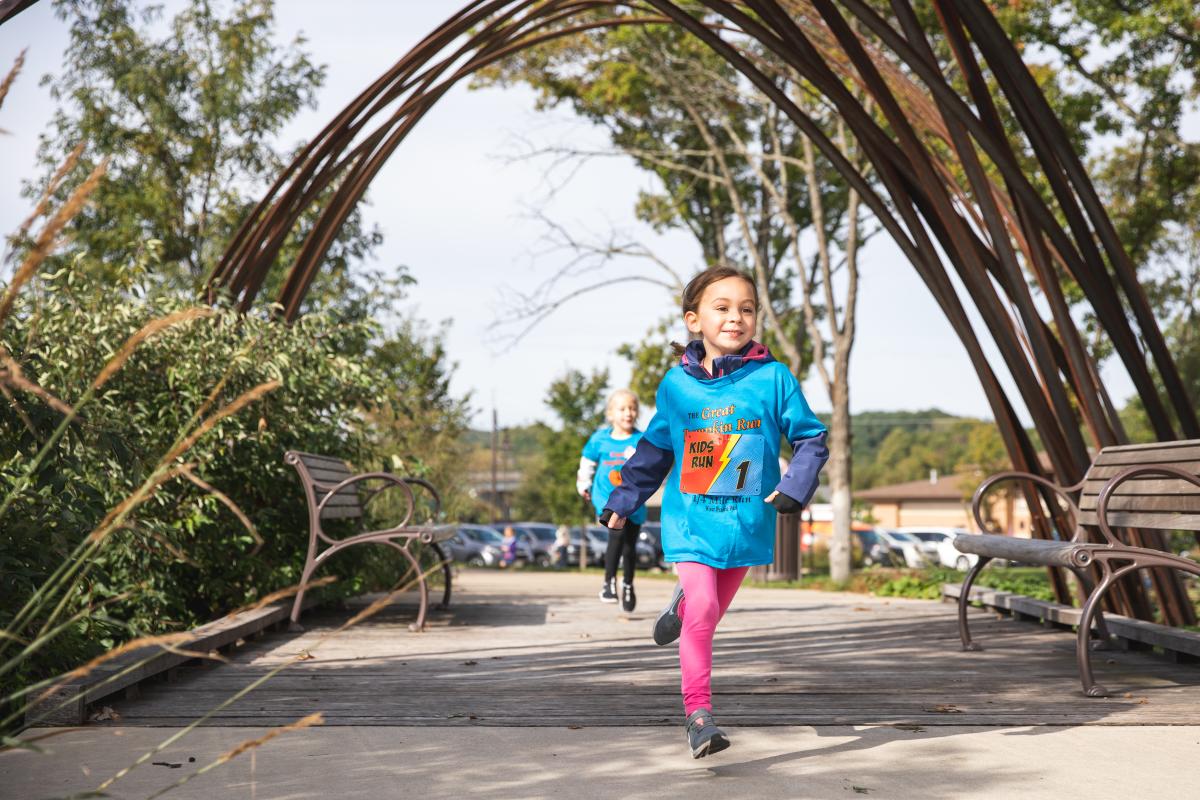 A young girl running under the arches in River Prairie at the Giant Pumpkin Run