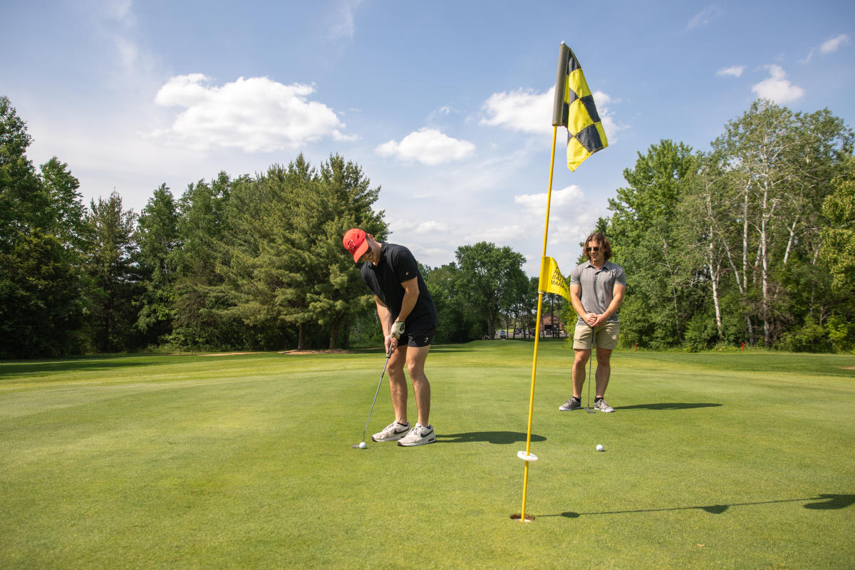 Two guys putting at a hole at Hickory Hills