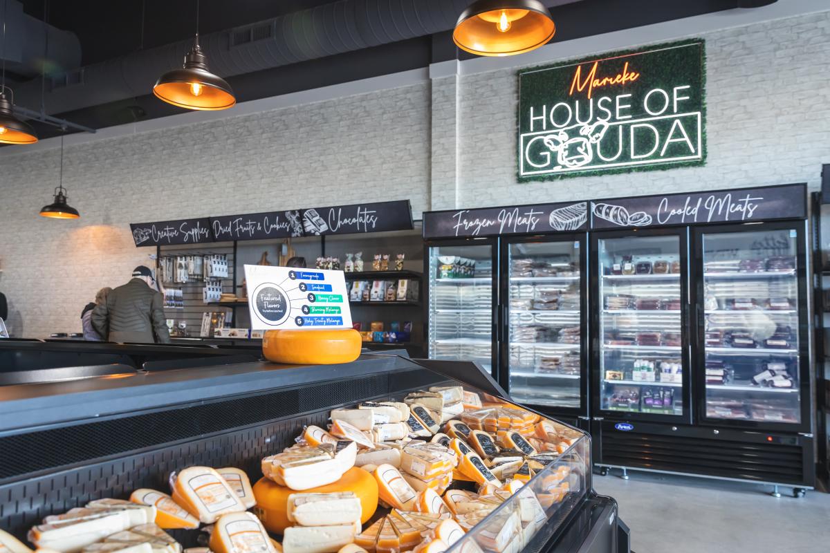 a photo of a freezer filled with cheese and a neon sign that says House of Gouda