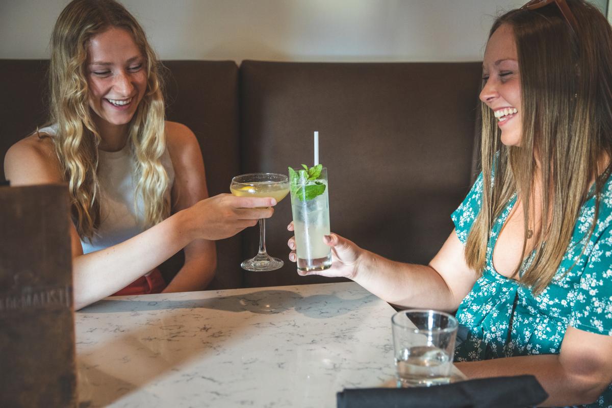 Two girls clinking their cocktail glasses together at The Informalist