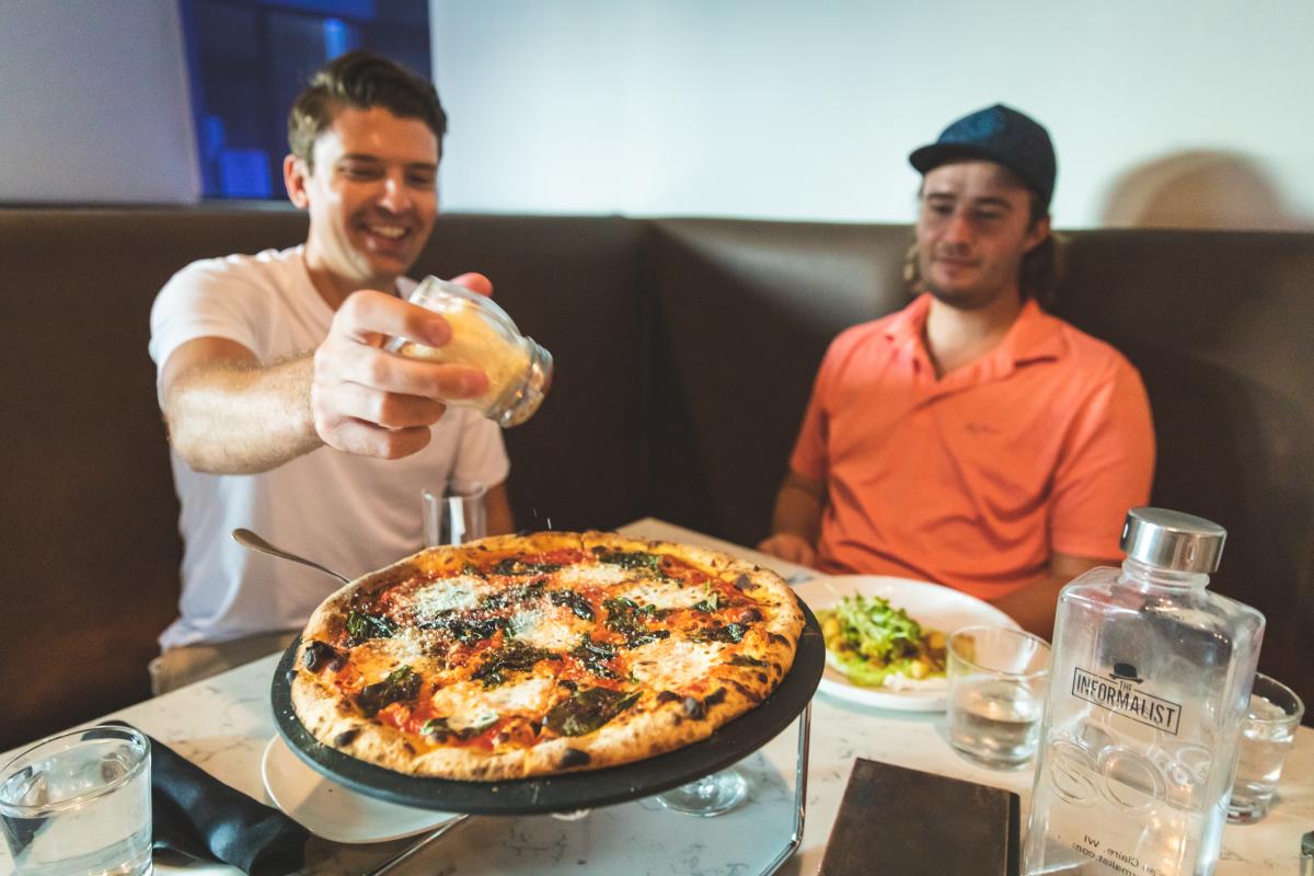 two guys sprinkling cheese over a pizza at the Informalist