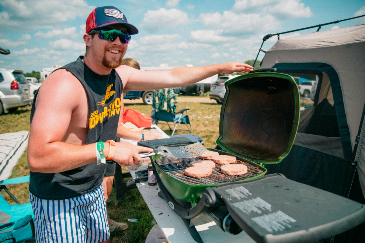 A guy grilling burgers at his campsite at the festival