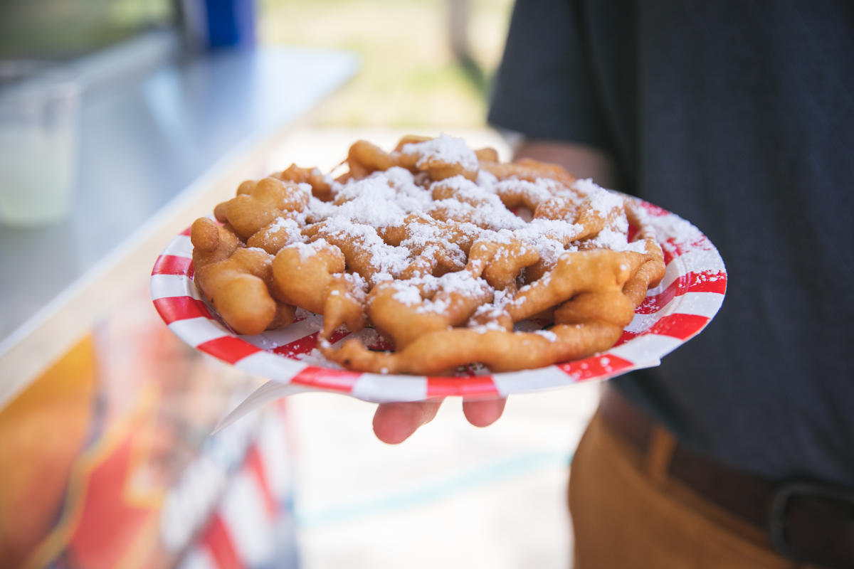 A hand holding a funnel cake on a plate