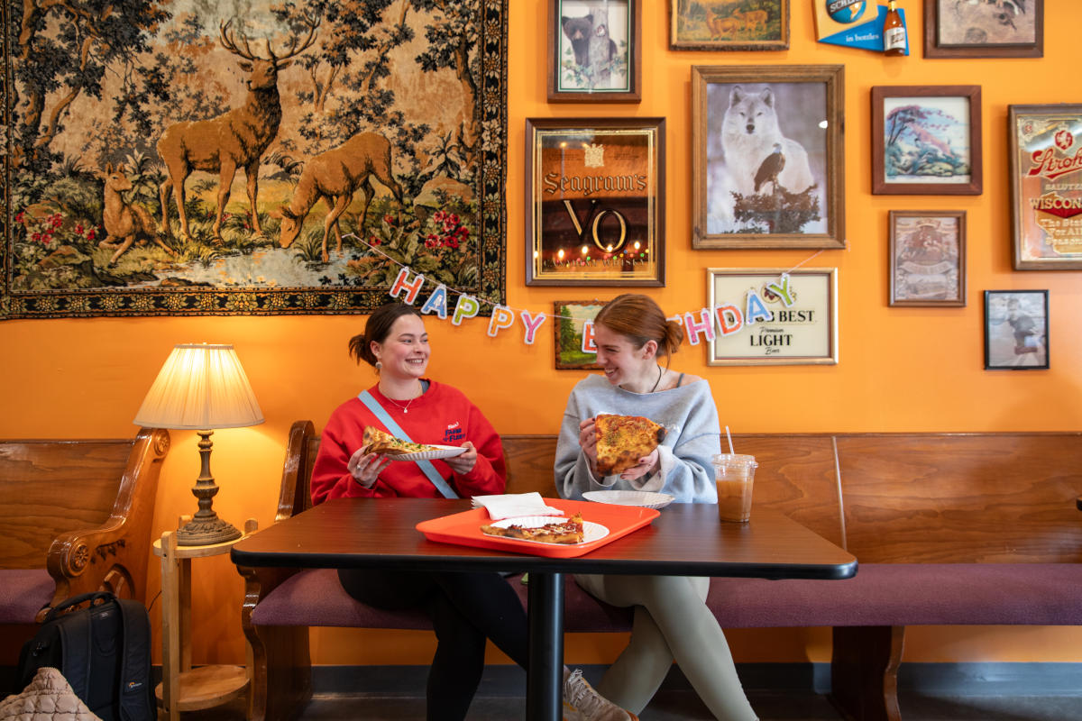 Two girls laughing and eating pizza at Leona's