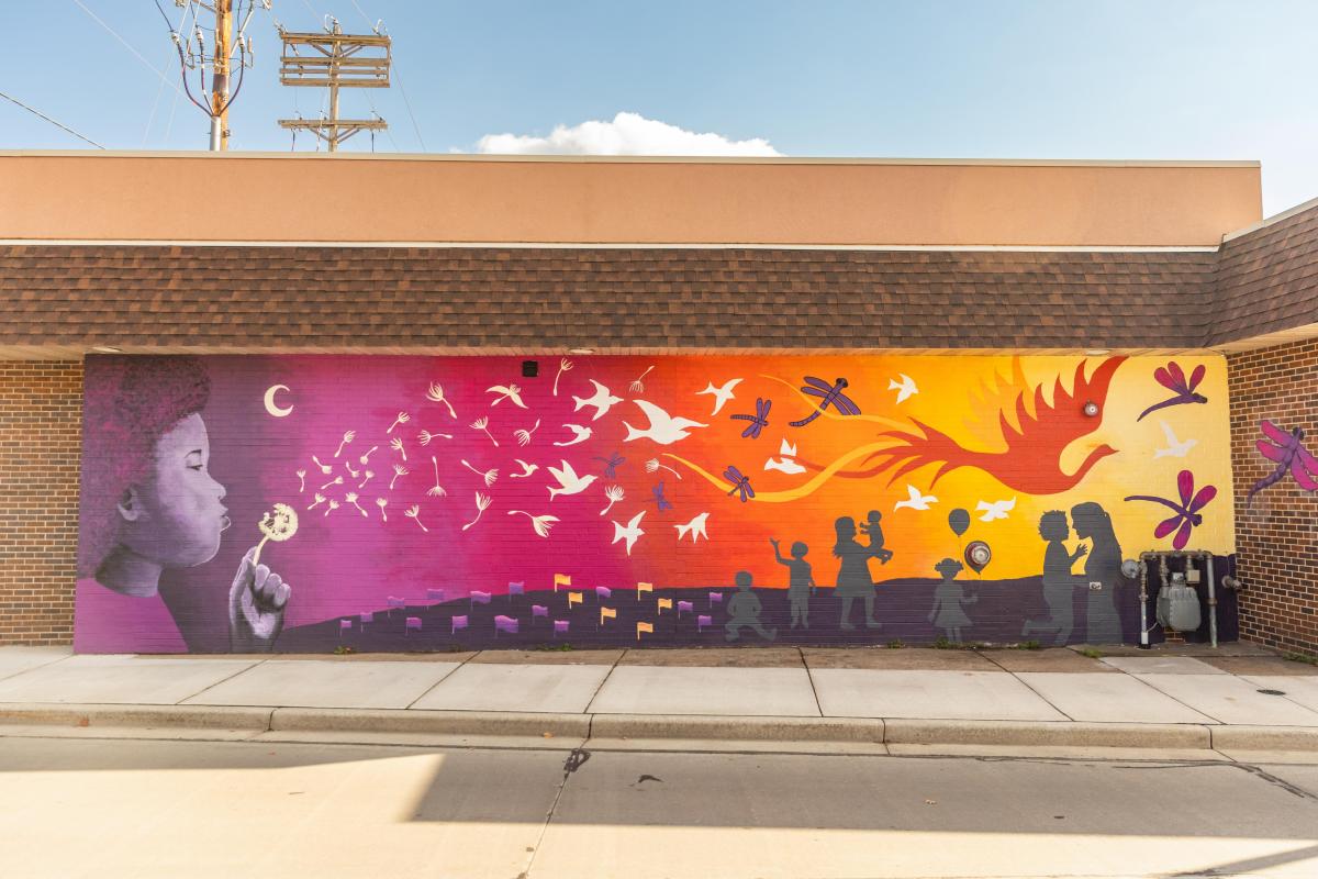A colorful sunset ombre mural of a kid blowing the seeds off a dandelion