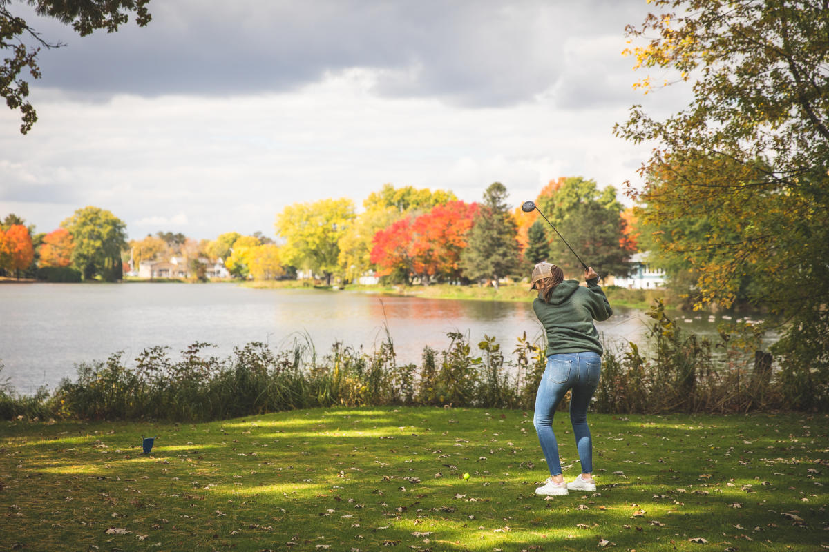 a girl playing golf by the colorful fall trees at Osseo Golf Club