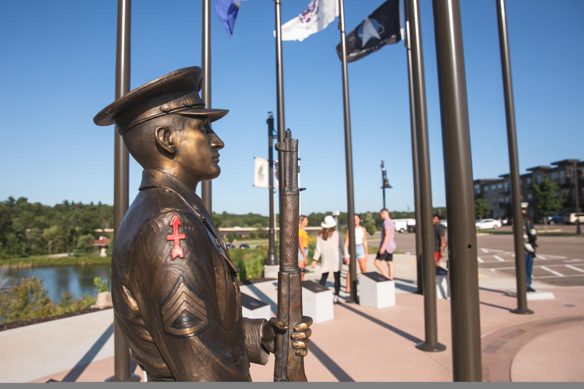 A sculpture of a war veteran and flags at the Veterans Tribute trail at River Prairie
