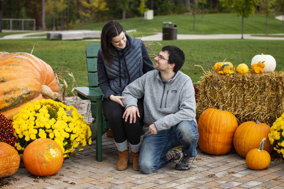 Couple sitting next to pumpkins and hay bales enjoying fall in River Prairie