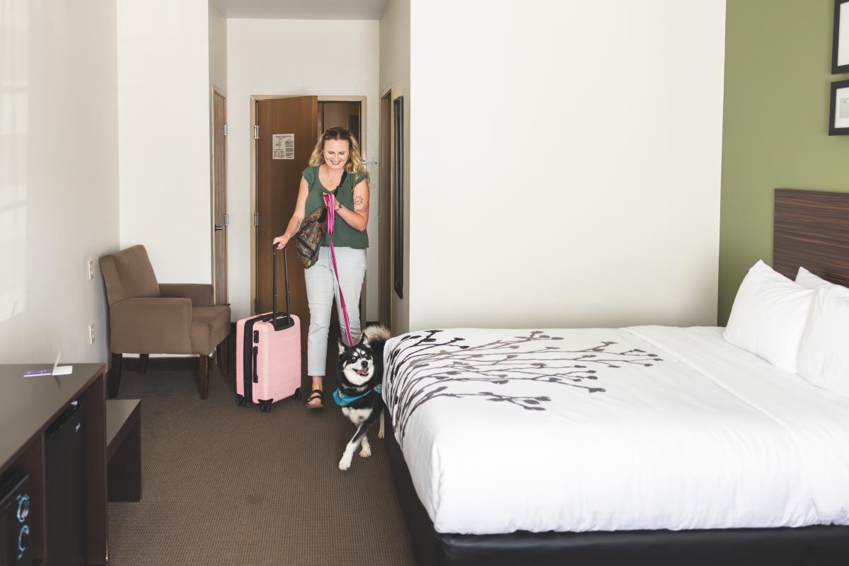 A guest at Sleep Inn & Suites in the Town of Wheaton walking into her room with a suitcase and her dog