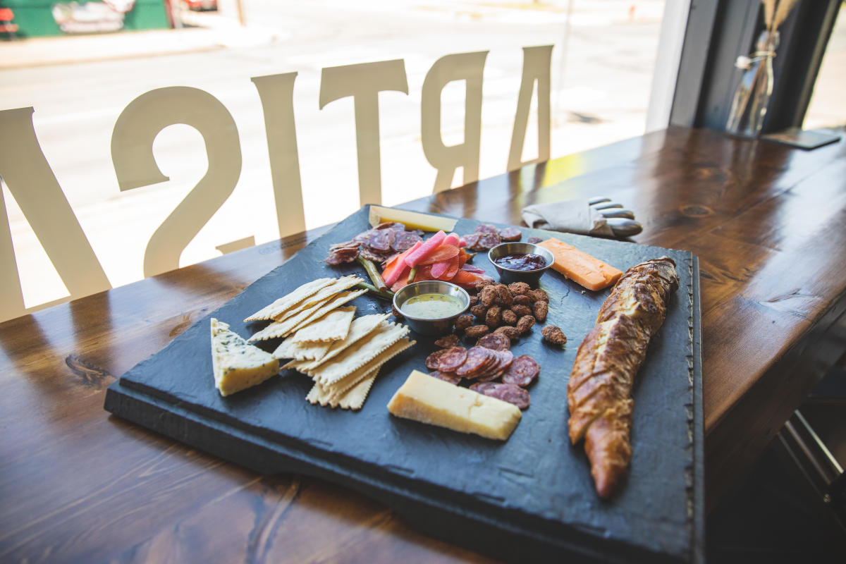 A photo of a big cheese board with meat, bread, vegetables, and spreads