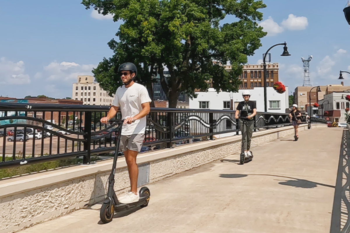 3 people riding electric scooters across a bridge in downtown Eau Claire