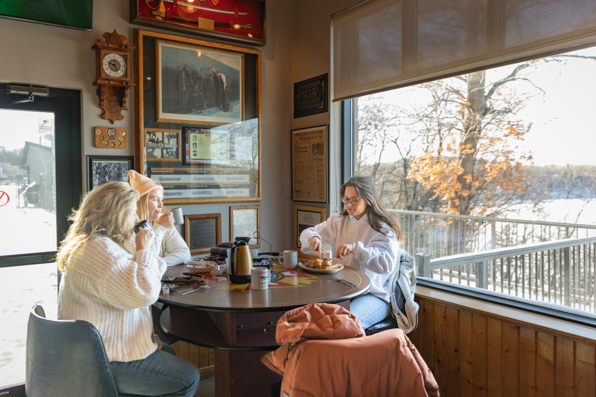 Three ladies sitting at a table by the window drinking coffee and eating breakfast