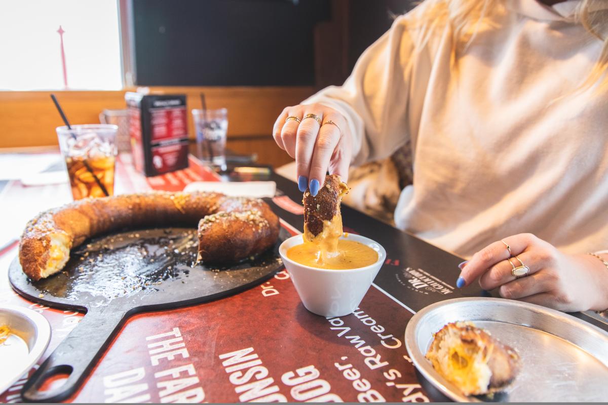 a girl dipping a stuffed pretzel into beer cheese dip at Wisco's