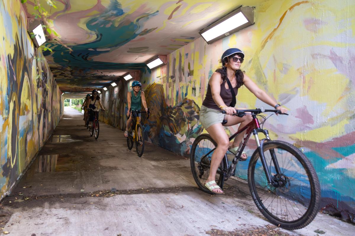 A group of women riding their bikes through a mural-painted tunnel