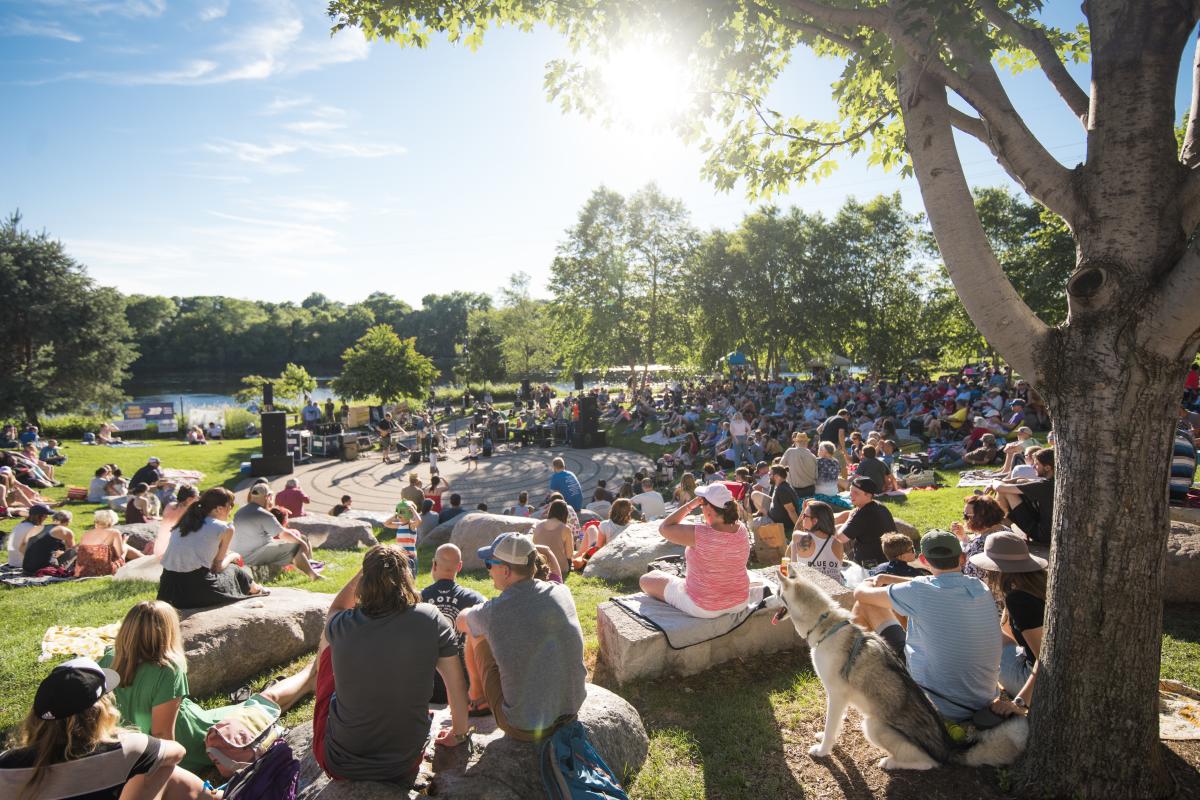 Small groups of people sitting on blankets on the ground at Sounds Like Summer Concert Series in Phoenix Park in downtown Eau Claire