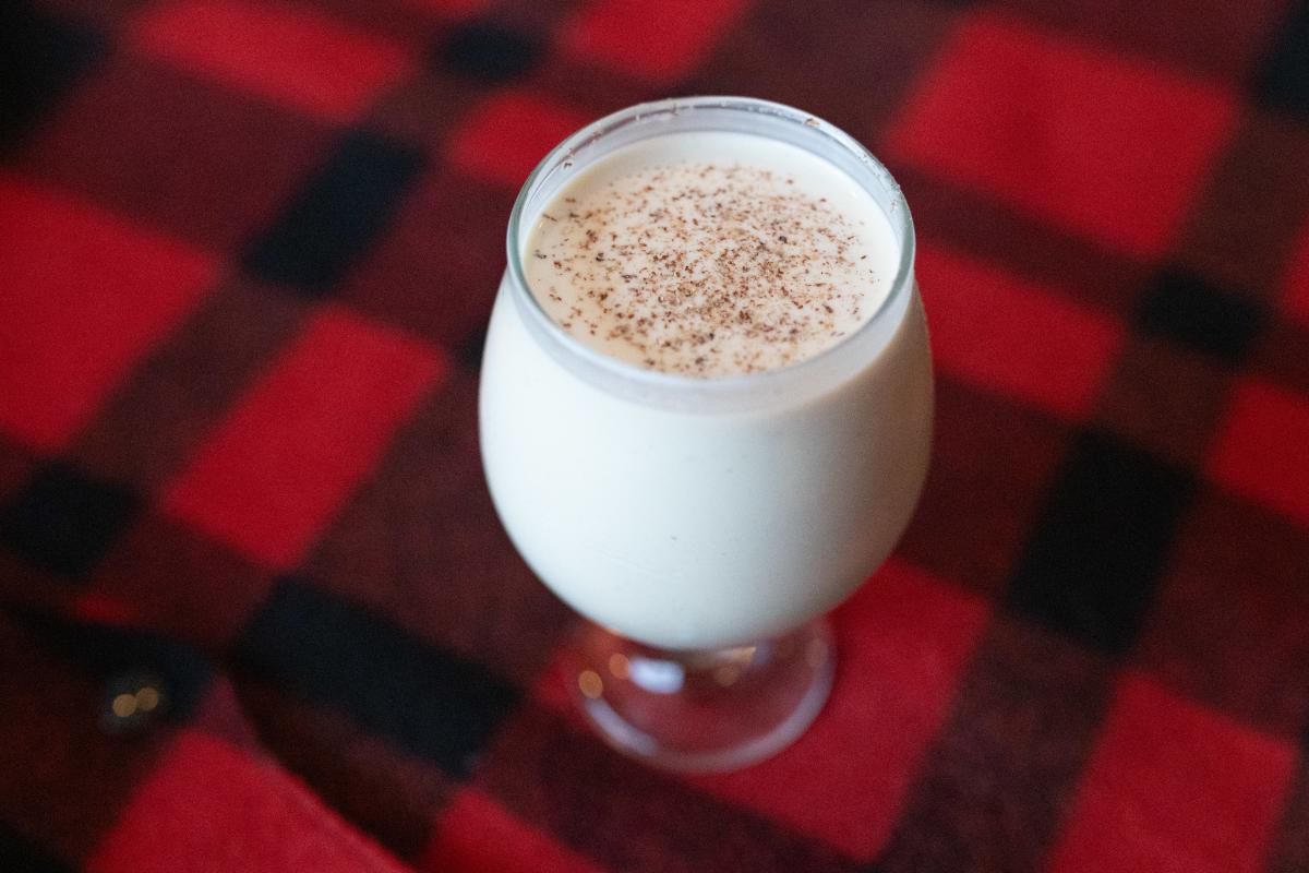a eggnog cocktail sitting on a red and black plaid blanket