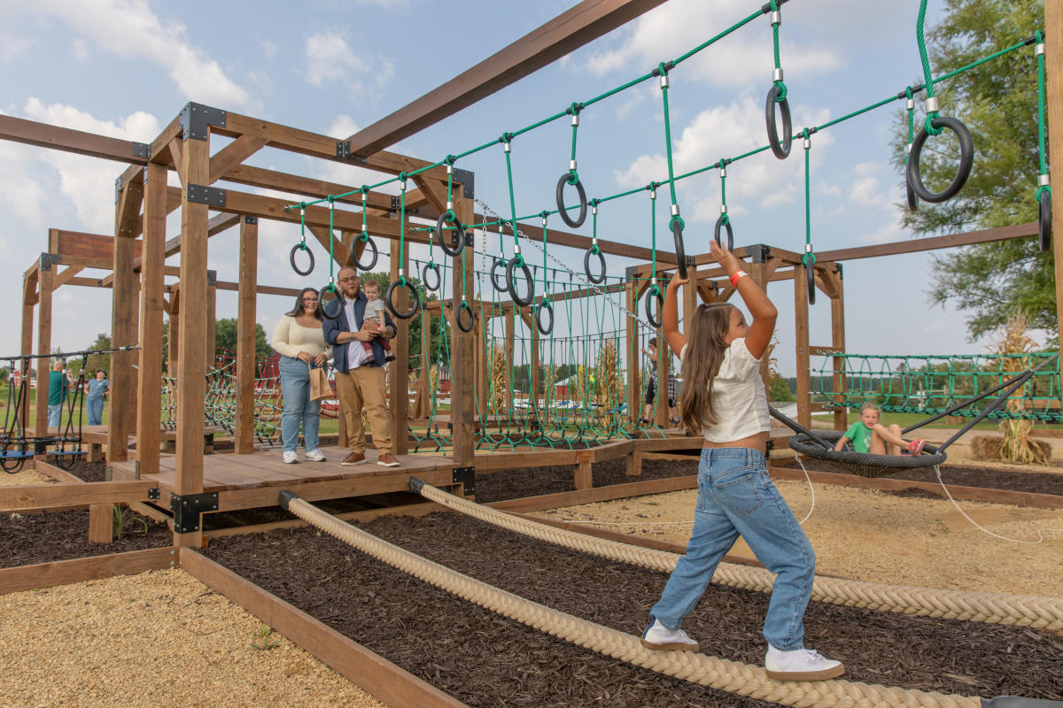 A young girl going through the ropes course while her family cheers her on at Ferguson's Orchards