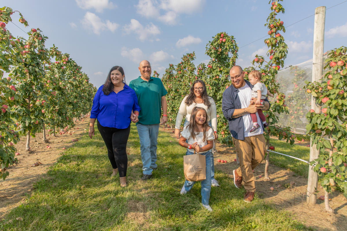 A family of parents, grandparents, and kids walking through the apple orchard at Ferguson's