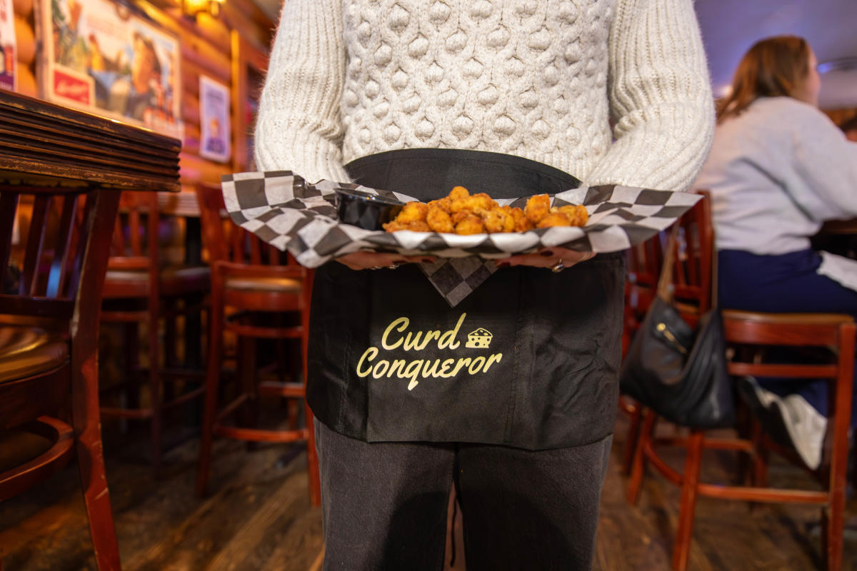 A girl wearing an apron and holding a platter of cheese curds