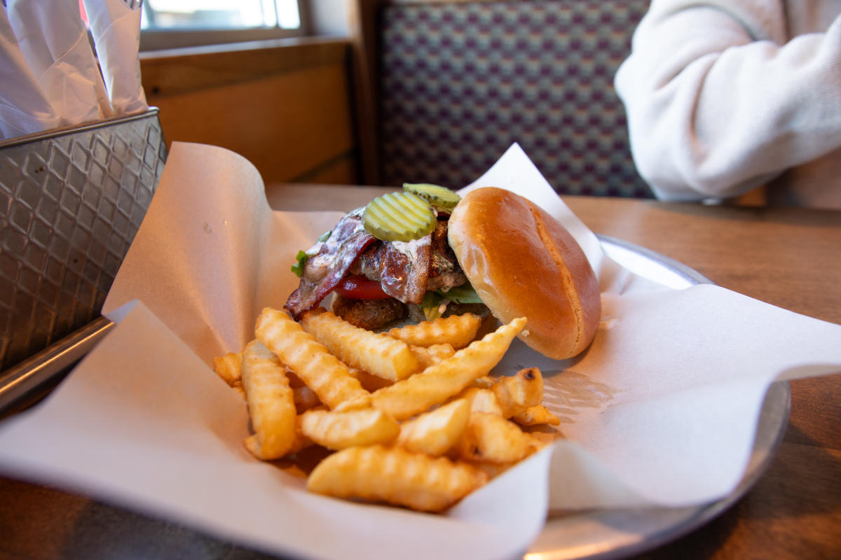 A burger loaded with pickles and bacon with fries