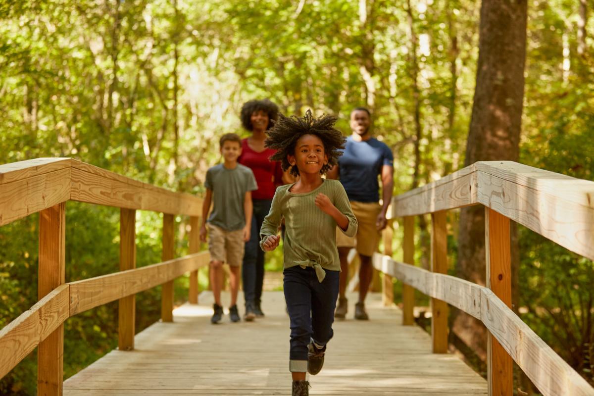 a family walking on a bridge with a little girl running toward the camera