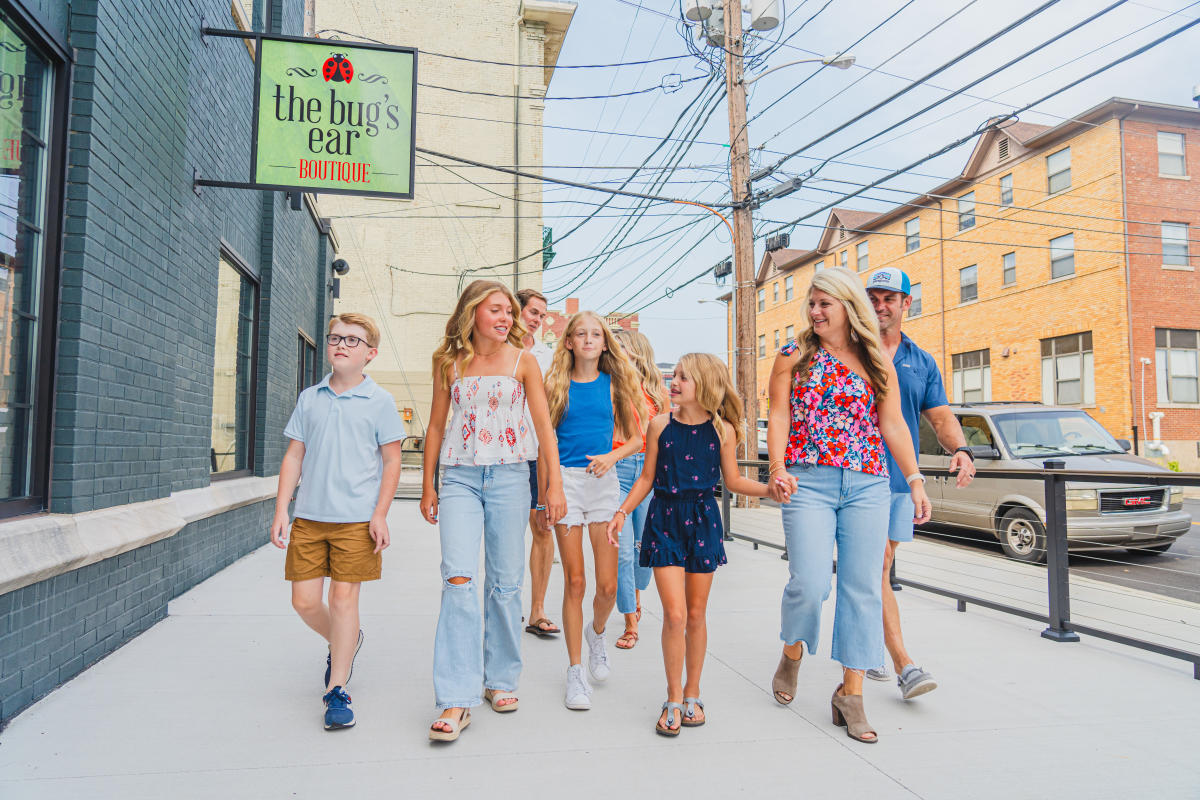 A group of people walking away from the bug's ear boutique sign in Downtown Elizabethtown