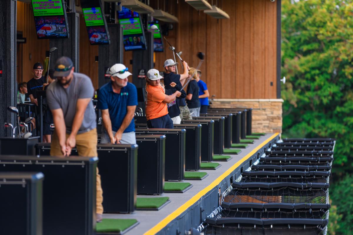 People swinging golf clubs at an outdoor bay at Cosmic Golf in Elizabethtown, KY.