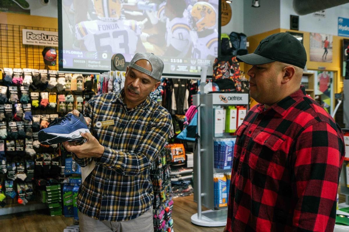 A man is talking to sales representative who is holding up a shoe in Running Soles in Downtown Elizabethtown