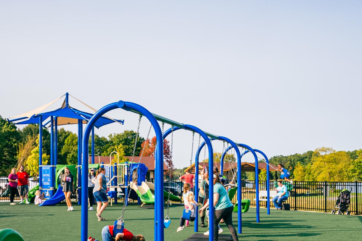 Children swinging on blue swings at a playground with rubberized flooring.