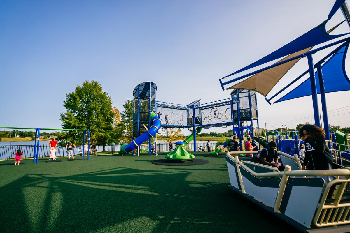 Playground with children enjoying slides and swings, featuring a large blue structure and shaded seating area