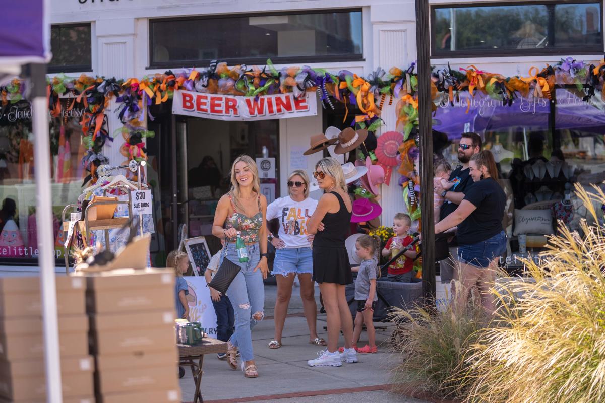 A group of people standing outside a decorated storefront with a "Beer Mine" banner, enjoying a lively outdoor event on a sunny day.