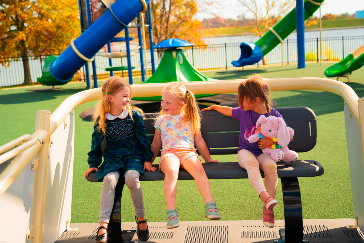 3 little girls sitting on a bench at the Oasis Playground at Freeman Lake Park in Elizabethtown, Kentucky