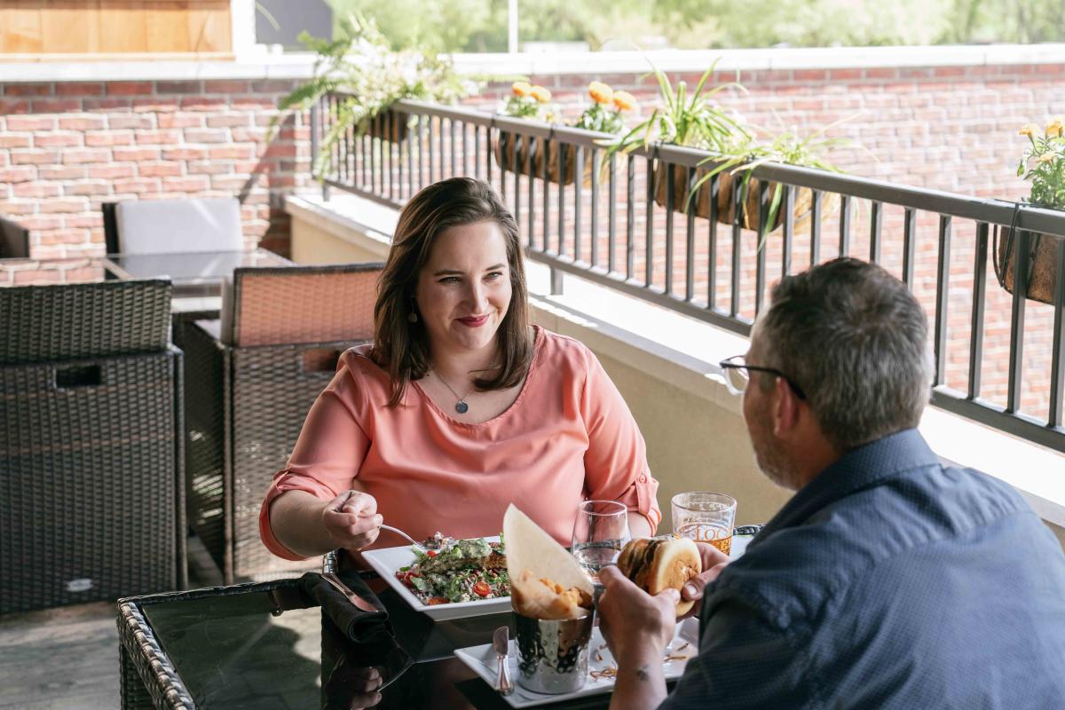 A woman smiling at the man seated across from her on the patio at J.R. Neighbors, while they are eating their food