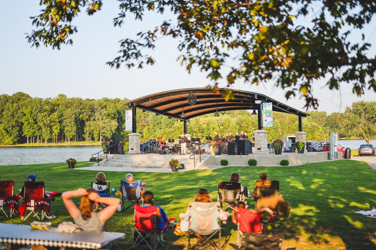 People are sitting in lawn chairs at Freeman Lake listening to a band at the Lawn Party in Elizabethtown, Kentucky