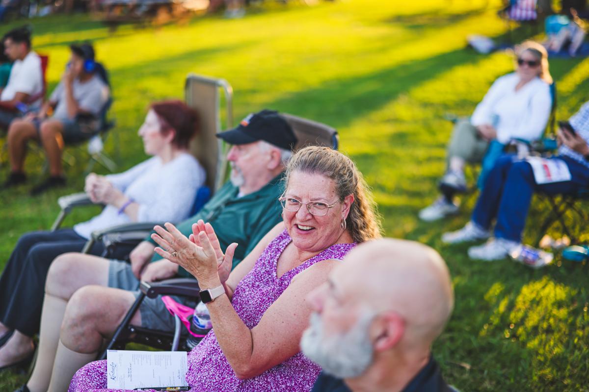 People are sitting in lawn chairs at Freeman Lake listening to a band at the Lawn Party in Elizabethtown, Kentucky