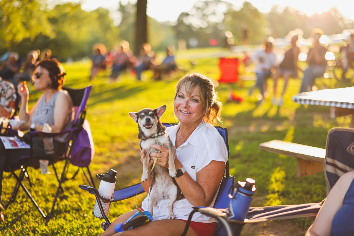 A lady smiling while sitting in a lawn chair holding up her dog at the Lawn Party in Elizabethtown, Kentucky