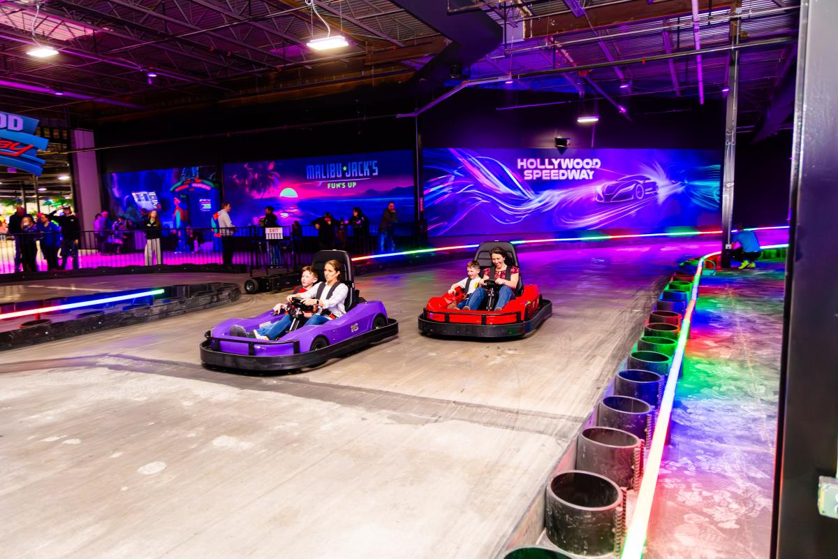 Indoor go-kart track with two colorful karts racing side by side under vibrant lighting at Hollywood Speedway.