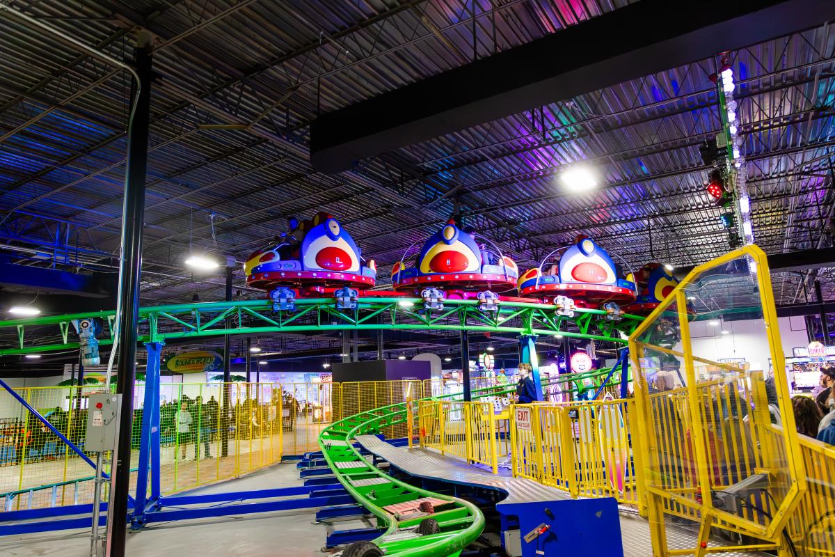 Indoor roller coaster with colorful cars and bright lighting inside an entertainment center.