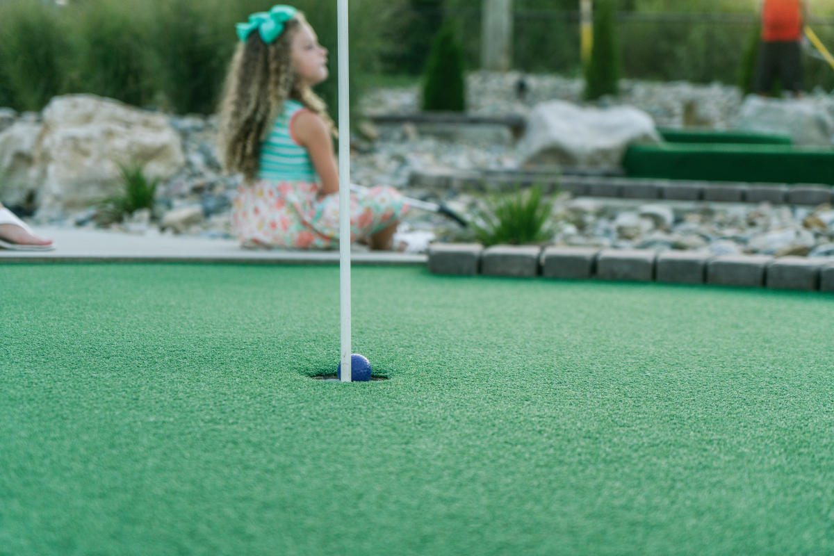a little girl sitting at mini golf green