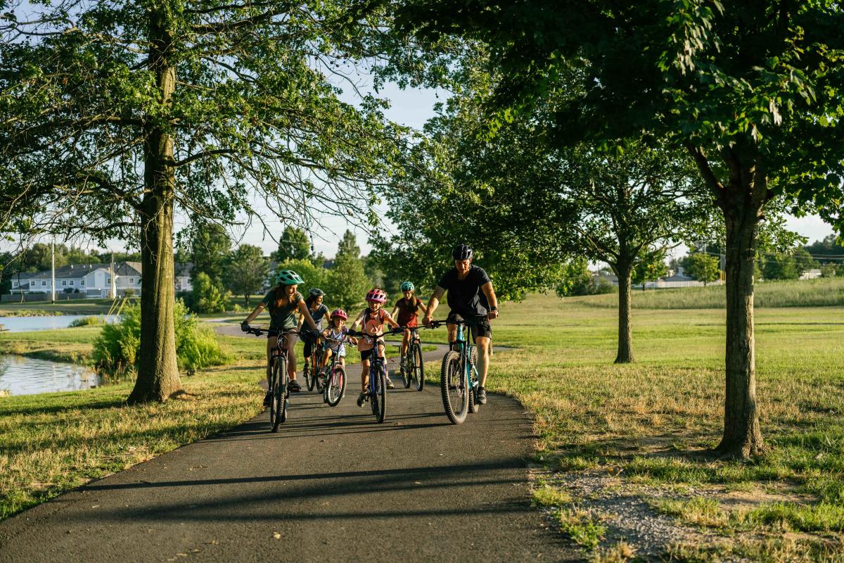 A group of people, including children, riding bicycles together on a paved path in a scenic park during a sunny day.