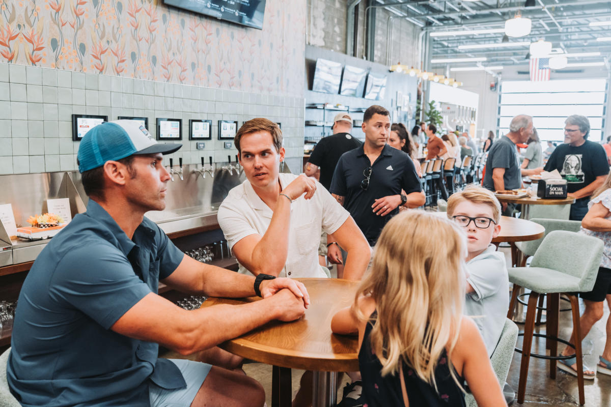 Two men, a young boy, and a young girl sitting at a table inside of the food court at Social on Main in Downtown Elizabethtown