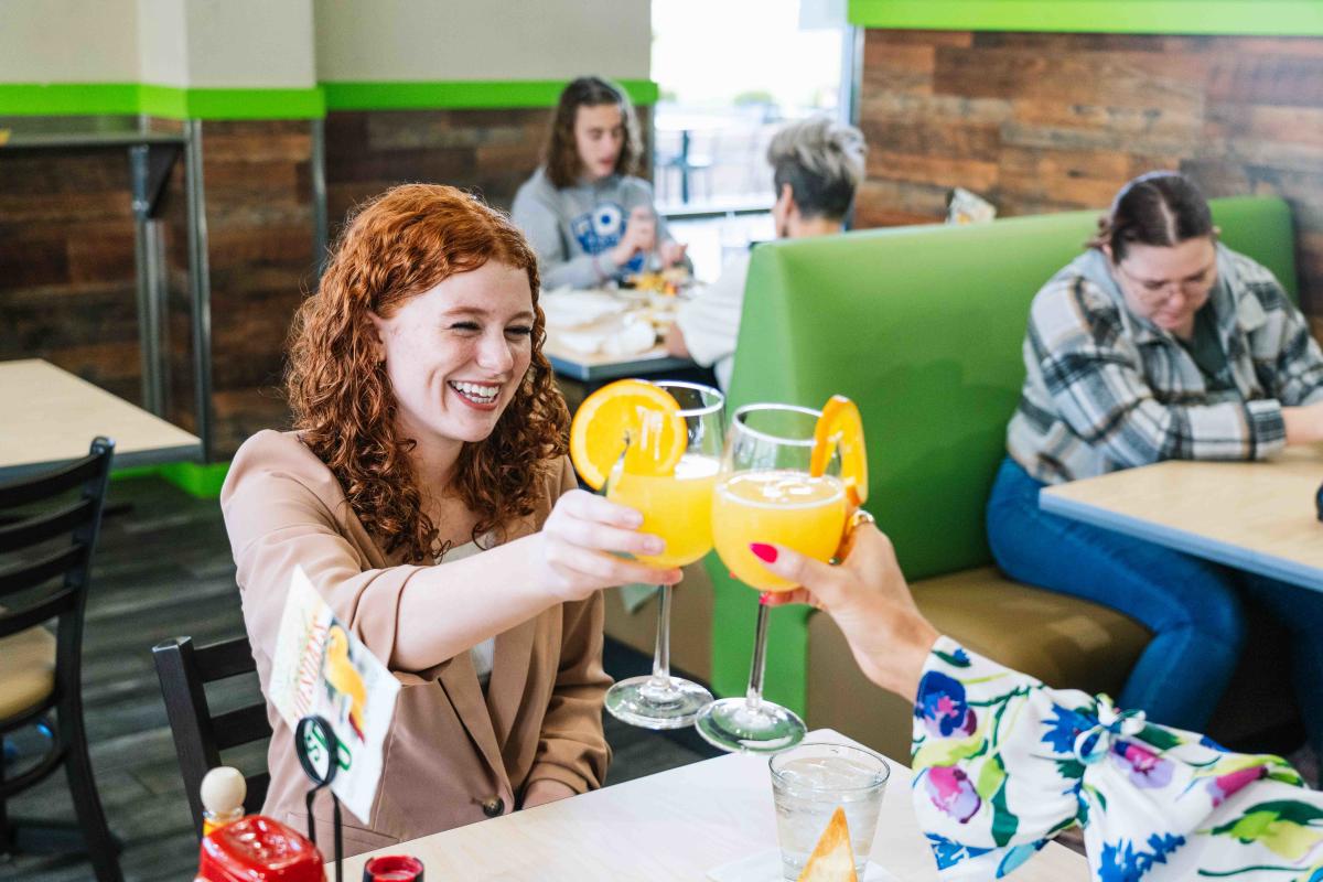 Two women raising their glasses of mimosas up for a "cheers" while dining at the Toasted Yolk in Elizabethtown, Kentucky