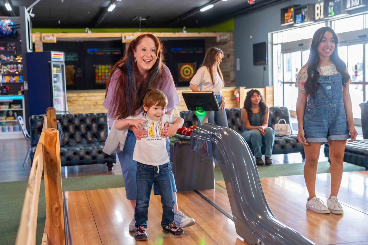 A young boy and a woman are standing on the bowling alley lane, getting ready to bowl at Xtreme Arcade