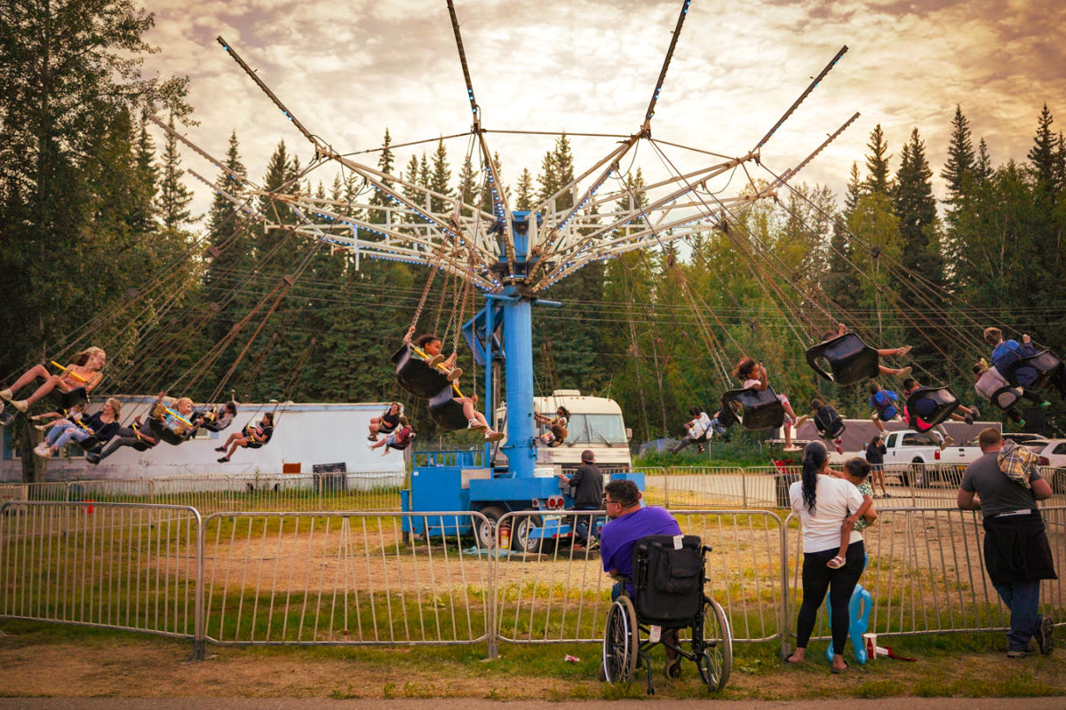 People swing through the air on a spinning carnival ride at the Tanana Valley State Fair while spectators watch from below.