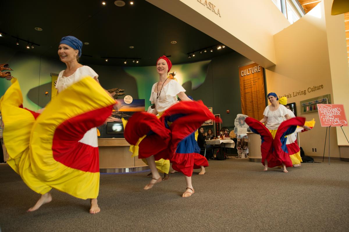 People happily dancing in flowy, vibrant skirts at the Fairbanks Summer Arts Festival.
