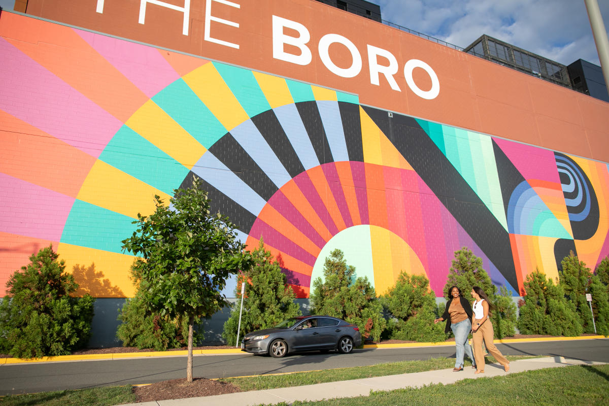 Two women walking in front of a mural
