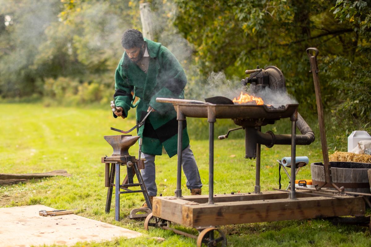 A man bent over and looking at his blacksmithing duties.
